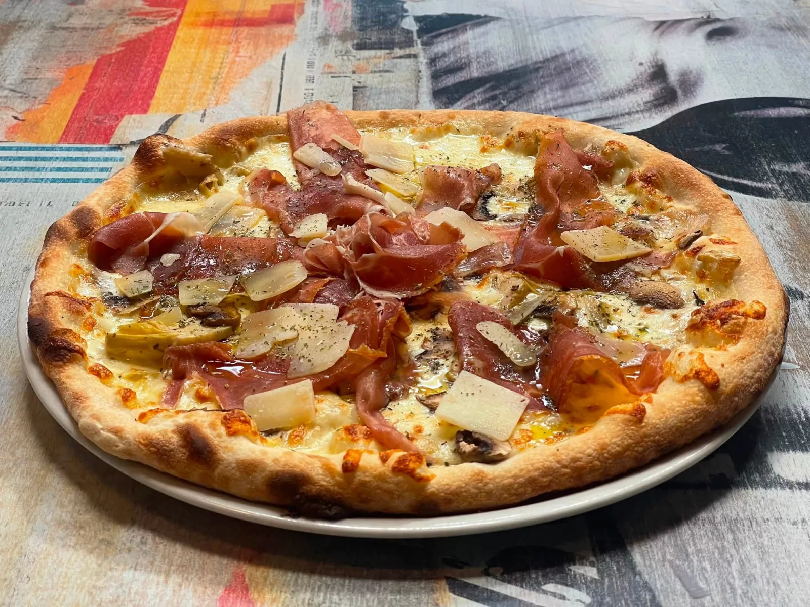 Pizza mozzarella, jambon cru, champignons, artichauts, copeaux de parmesan, origan italien