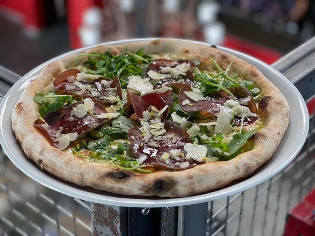 Pizza : Mozzarella, roquette, viande séchée, copeaux de parmesan, zeste de citron, émulsion d'huile d'olive citron et poivre.