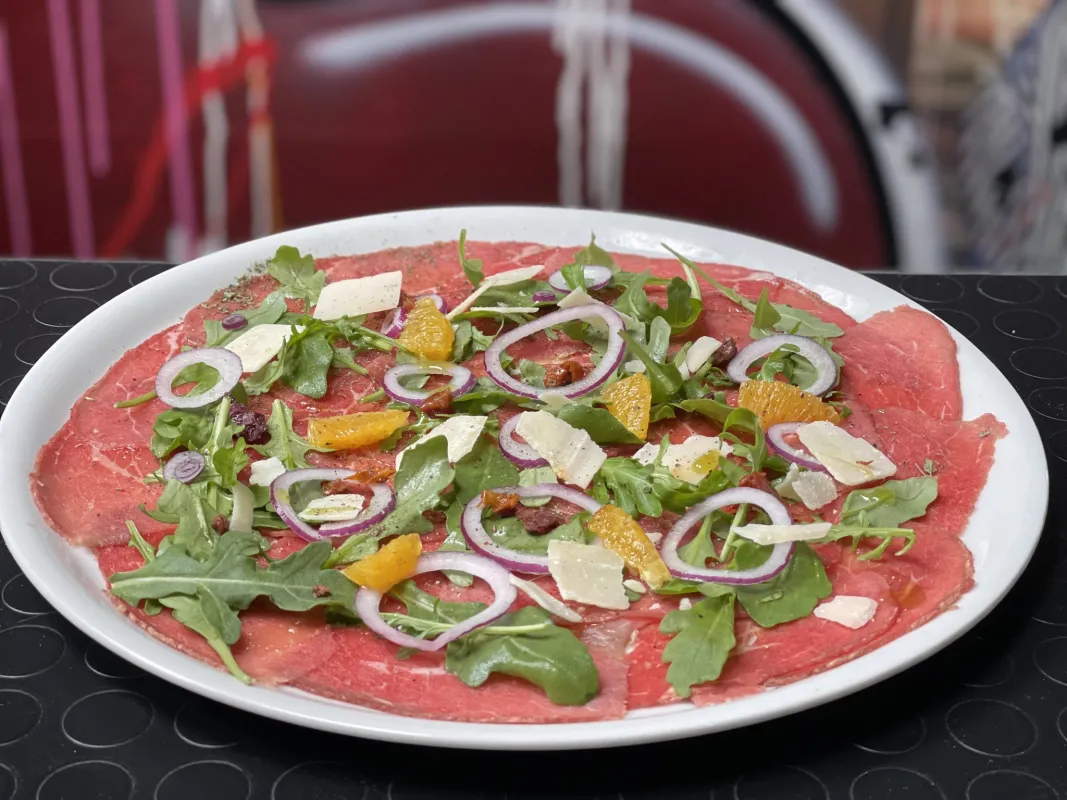 Carpaccio de bœuf, copeaux de parmesan, rucola, oignons, tomates séchées, suprême d'orange