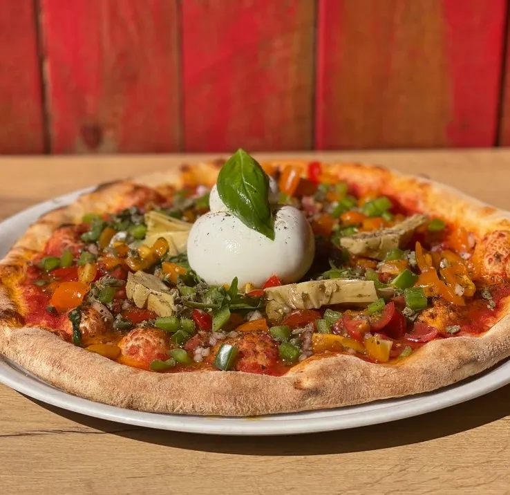 Pizza avec tomate, origan, huile d'ail, rucola, artichauts grillés, tomates concassées, poivrons, câpres, oignons, burrata