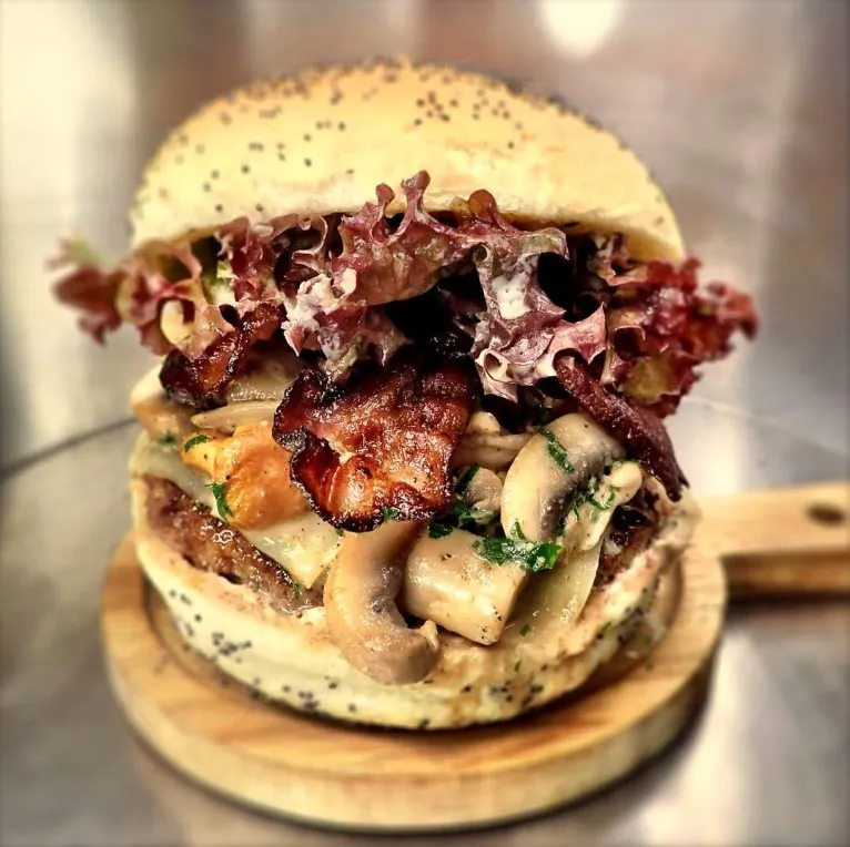 Burger Champiz : Bun artisanal de notre boulanger (CH), steak BEEFORE ( 150g bœuf/veau, CH), fricassée de champignons à la crème (chanterelles, pleurottes, Paris), raclette de Bagnes (VS), bacon grillé (CH), salade et mayo maison aïoli